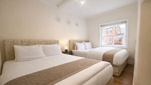 Une chambre d’hôtel avec deux lits, une fenêtre donnant sur un immeuble en briques rouges et un luminaire au plafond.