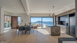 Una cocina moderna con una isla grande, un comedor con sillas y vista al mar.