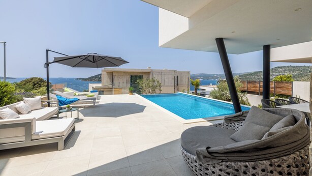 Zona de piscina exterior moderna con sillas de descanso y una sombrilla grande, con vistas a un paisaje pintoresco.