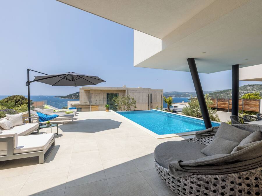 A modern outdoor pool area with lounge chairs and a large umbrella, overlooking a scenic landscape.