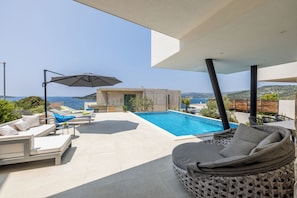 Zona de piscina exterior moderna con sillas de descanso y una sombrilla grande, con vistas a un paisaje pintoresco.