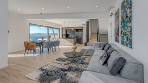 Una sala de estar moderna con un sofá gris, un comedor con mesa y sillas, y una cocina al fondo.