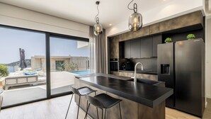 Una cocina moderna con una isla grande, electrodomésticos de acero inoxidable y vistas a una piscina y al paisaje urbano.