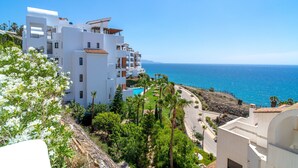 A coastal building with multiple balconies overlooking the sea, a swimming pool, and lush greenery.