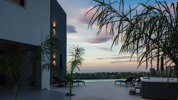 A modern outdoor terrace with a pool, lounge chairs, and a hot tub, overlooking a cityscape at dusk. - Grand Luxe Villa - Sea views, hot tub, private pool & modern design (Chania)