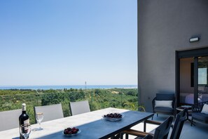 A terrace with a table set for dining, a bottle of wine, and a bowl of fruit.