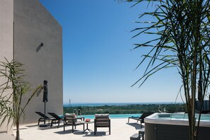 A rooftop terrace with lounge chairs, a hot tub, and a view of the ocean.