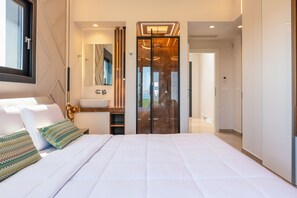 A modern bedroom with a large bed, a bathroom with a glass shower door, and a view of the outside.
