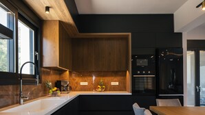 A modern kitchen with a wooden accent wall, a white countertop, and a built-in oven. - Grand Luxe Villa - Sea views, hot tub, private pool & modern design (Chania)