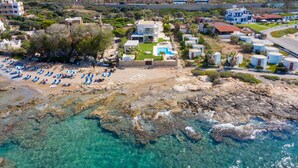 Eine Vogelperspektive einer Küstenlandschaft mit Strand, klarem Wasser und mehreren Gebäuden, darunter ein modernes Haus mit Schwimmbad.