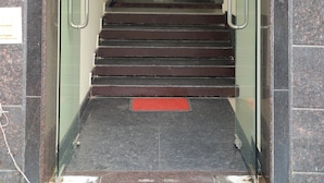 Entrada de hotel con puerta de vidrio, una escalera que conduce al interior y un felpudo rojo al final.