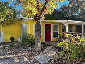 Un edificio giallo con una porta rossa, un piccolo portico e un albero di fronte.