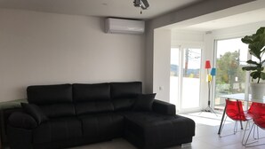 A modern living room with a black sectional sofa, a glass table with red chairs, and a large potted plant. - campagne de sitges (Olivella)