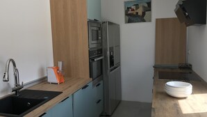 A modern kitchen with a stainless steel refrigerator, oven, and microwave. There is a wooden countertop and a sink with a faucet. A painting is on the wall above the oven. - campagne de sitges (Olivella)