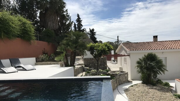 A swimming pool with clear water, surrounded by a patio with lounge chairs, a small garden, and a building with a tiled roof. - campagne de sitges (Olivella)