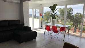 A modern living room with a black sofa, a glass table with red chairs, and a potted plant. - campagne de sitges (Olivella)