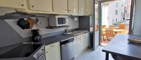 A compact kitchen with white cabinets, a microwave, and a dishwasher. There is a dining area with a table and chairs visible through an open door.