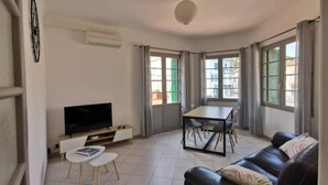 A living room with a TV, a dining table, and a sofa. - Appartement 2 Avec Emplacement Idéal et Clim (Collioure)