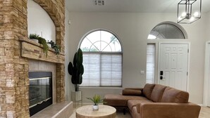 A living room with a fireplace, a brown sofa, two round wooden tables, and a large arched window. - Private and Charming Vacation Home near Downton Gilbert - Pool/hot tub/fireplace (Gilbert)