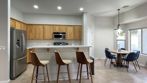 A modern kitchen with wooden cabinets, stainless steel appliances, a central island with bar stools, and a dining area with a table and chairs. - Private and Charming Vacation Home near Downton Gilbert - Pool/hot tub/fireplace (Gilbert)