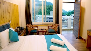 Habitación de hotel con una cama, una mesita con sillas, un ventanal con vista a la ciudad y una puerta que da a un balcón.