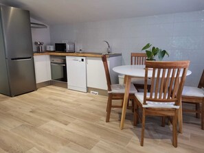 Cocina compacta equipada con refrigerador, microondas, lavavajillas y mesa de comedor de madera con sillas.