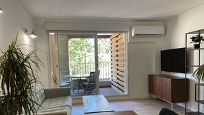 A modern living room with a sofa, a dining table, and a TV. - T2 Bord du Canal du Midi Piscine (Homps)