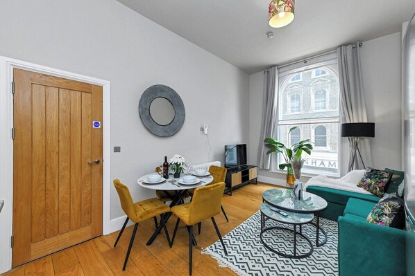 A modern living room with a dining area, a sofa, a TV, and a window with a view of a building. - 1 Bed Apt Next to Market Square & Transport Links (Nottingham)