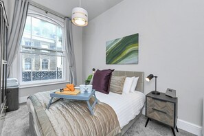 Ein Schlafzimmer mit Bett, Nachttisch, Lampe und einem Fenster mit Vorhängen.