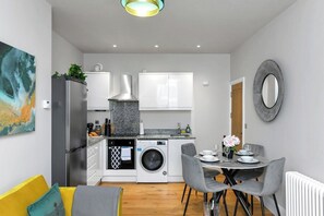 A compact kitchen with a washing machine, a dining area with a table and chairs, and a sofa. - 1-Bed City Flat Close to Market Square & Transport (Nottingham)