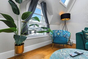 A room with a large window, a blue chair, a green sofa, a floor lamp, and a potted plant. - 1-BR City Centre Flat – Steps from Market Square (Nottingham)