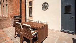 A wooden outdoor seating area with a table and chairs, a clock on the wall, and a dark door. - Wow! 1bed Stunning Apt in Victorian Mansion (Nottingham)