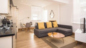 A modern living room with a grey sofa, a coffee table, and a dining area with chairs and a table. - Wow! 1bed Stunning Apt in Victorian Mansion (Nottingham)