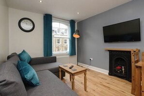 A living room with a sofa, a coffee table, a fireplace, a TV, and a window with curtains.