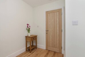 Ein Flur mit einer Holztür, einem kleinen Holztisch mit Blumenvase und einem Lichtschalter an der Wand.