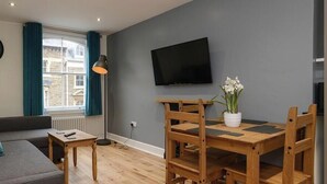 Ett vardagsrum med en soffa, ett litet bord, en tv och en matplats med stolar och ett bord.