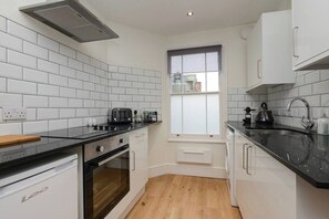 Eine moderne Küche mit weißen Schränken, schwarzen Arbeitsflächen, einem Fenster und einem eingebauten Backofen.