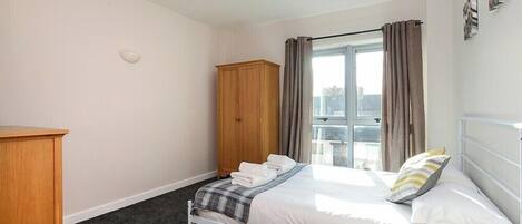 A bedroom with a bed, a wardrobe, a window with curtains, and a view of the outside.