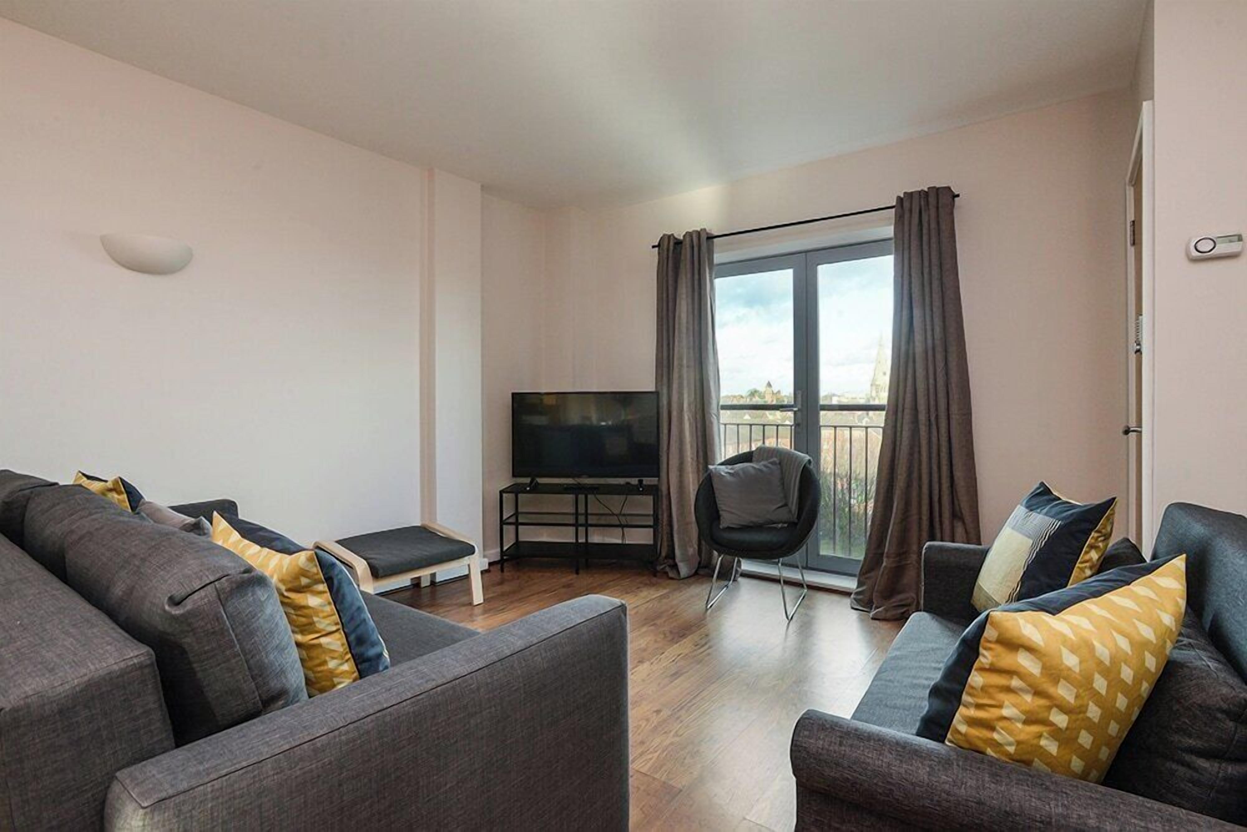 A modern living room with grey sofas, a flat-screen TV, and a balcony with curtains.