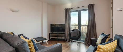 Ett modernt vardagsrum med grå soffor, en platt-TV och en balkong med gardiner.