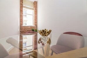 A modern room with a glass table, two chairs, a decorative vase, and a brick wall with a window. - Lovely 1 Bedroom Apartment at City Centre (Nottingham)
