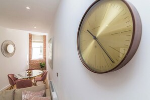 A wall-mounted clock, a dining area with a glass table, and a brick wall. - Lovely 1 Bedroom Apartment at City Centre (Nottingham)