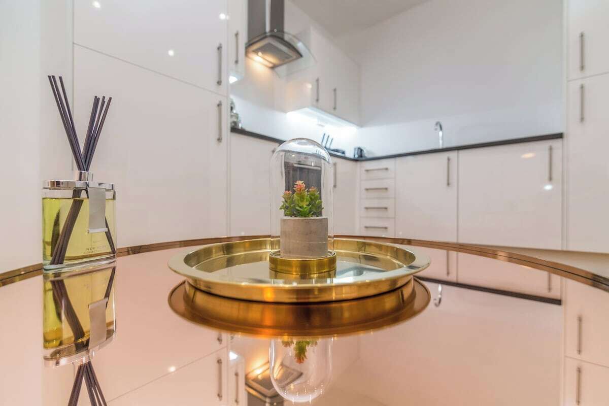 A modern kitchen with white cabinets, a central island with a glass top, and a small potted plant.