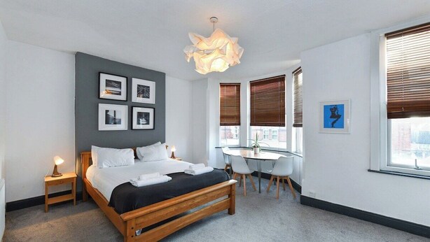 Een moderne hotelkamer met een houten bed, een bureau en een groot raam met jaloezieën.