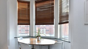 Een vergaderruimte met een ronde tafel, twee witte stoelen en een plant in een pot.