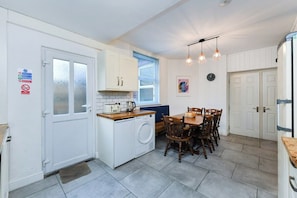 A compact kitchen with a washing machine, a dining table with chairs, and a refrigerator. - 5-BR Home Featuring Art and Photography Collection (Nottingham)