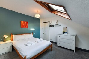 A bedroom with a bed, bedside table, dresser, and a skylight.