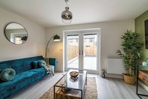 A living room with a teal sofa, a glass coffee table, a mirror, and a potted plant.