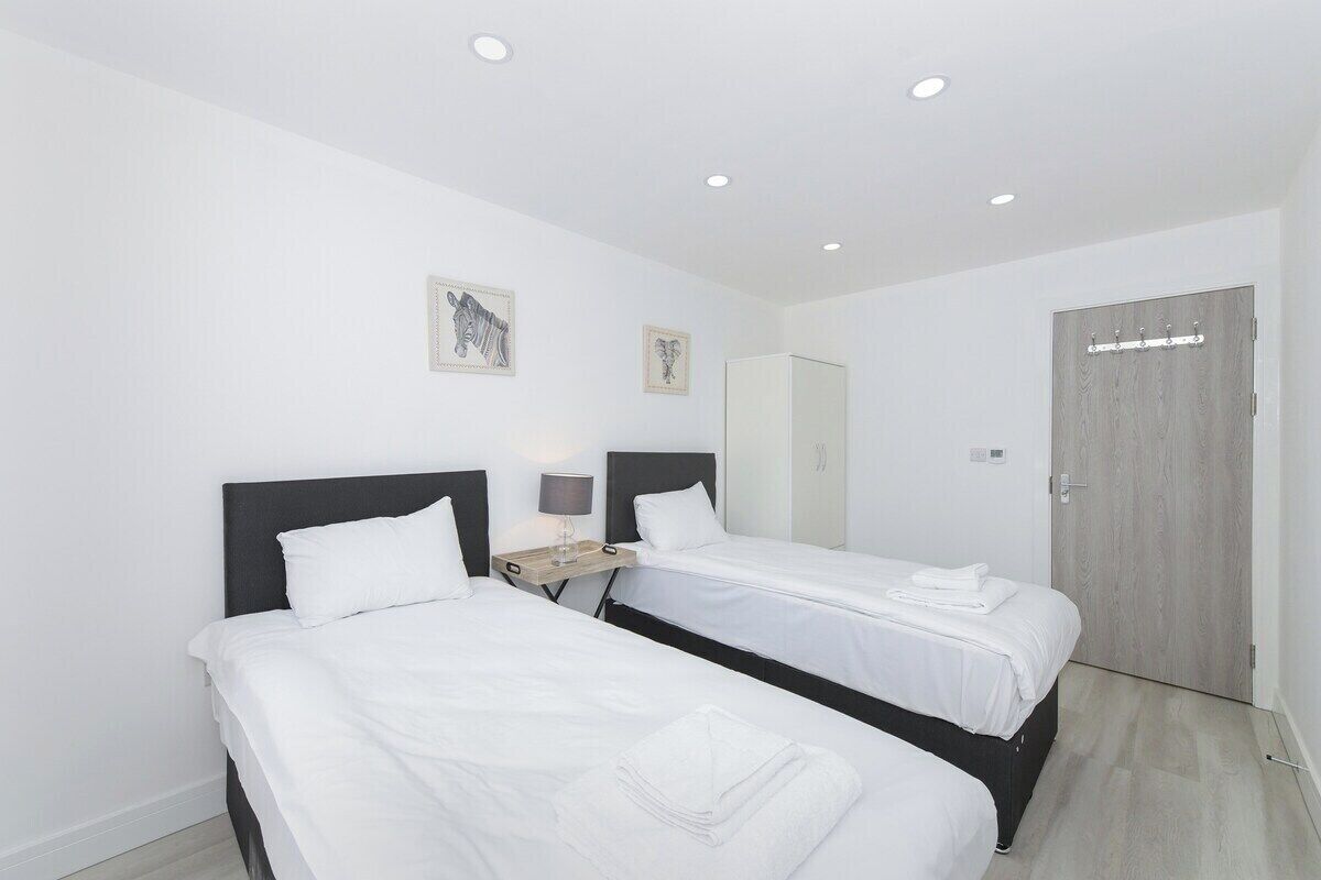 A hotel room with two single beds, a bedside table with a lamp, a wardrobe, and a door with a coat rack.