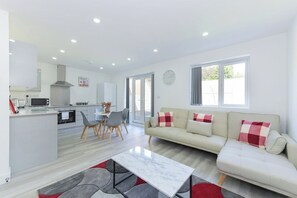 A modern kitchen with a dining area, a sofa with checkered cushions, and a clock on the wall. - 2-BR Apartment w/ Parking Near Nottingham (Gedling)